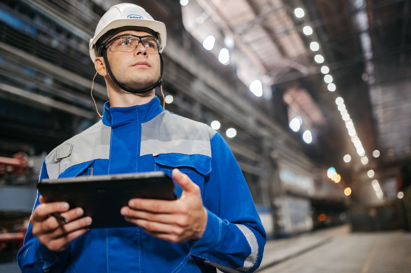 Engenheiro de capacete e uniforme consultando um tablet no chão de fábrica