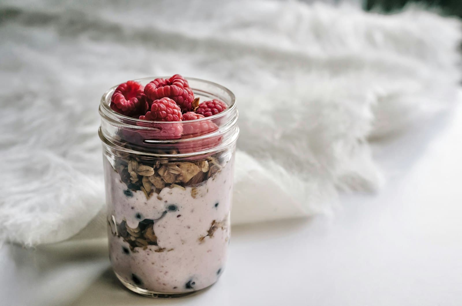 Overnight Oats im Glas mit Granola und Himbeeren