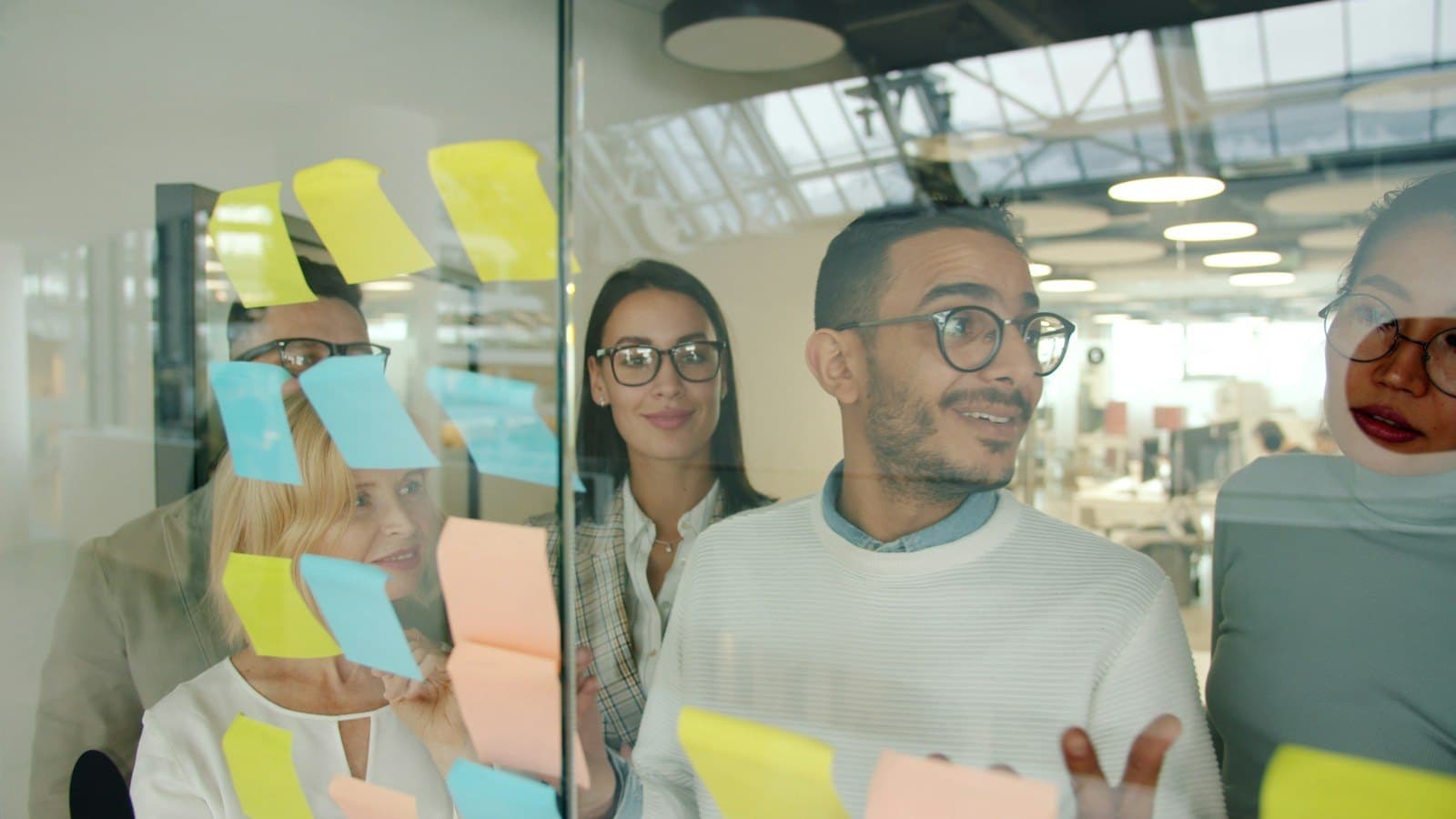 A young, diverse team working through ideas on a glass wall covered in sticky notes