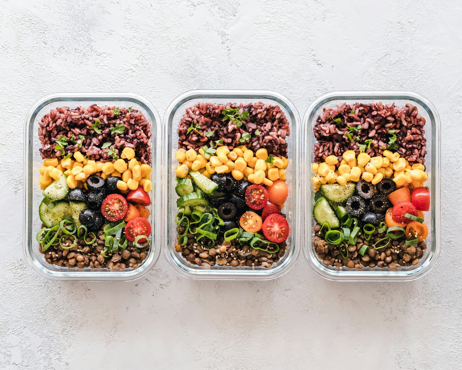 Drei Meal-Prep-Boxen mit Reis, Linsen und frischem Gemüse